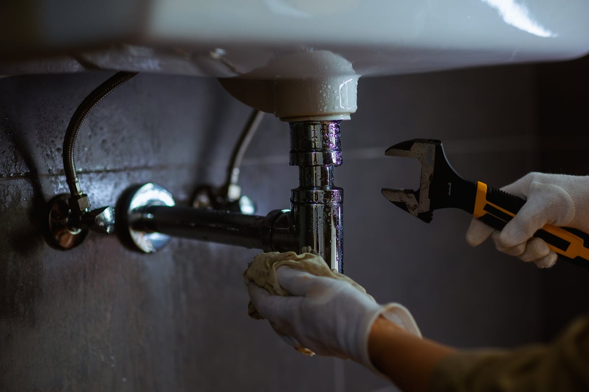 Clark's plumber repairing pipes under a sink