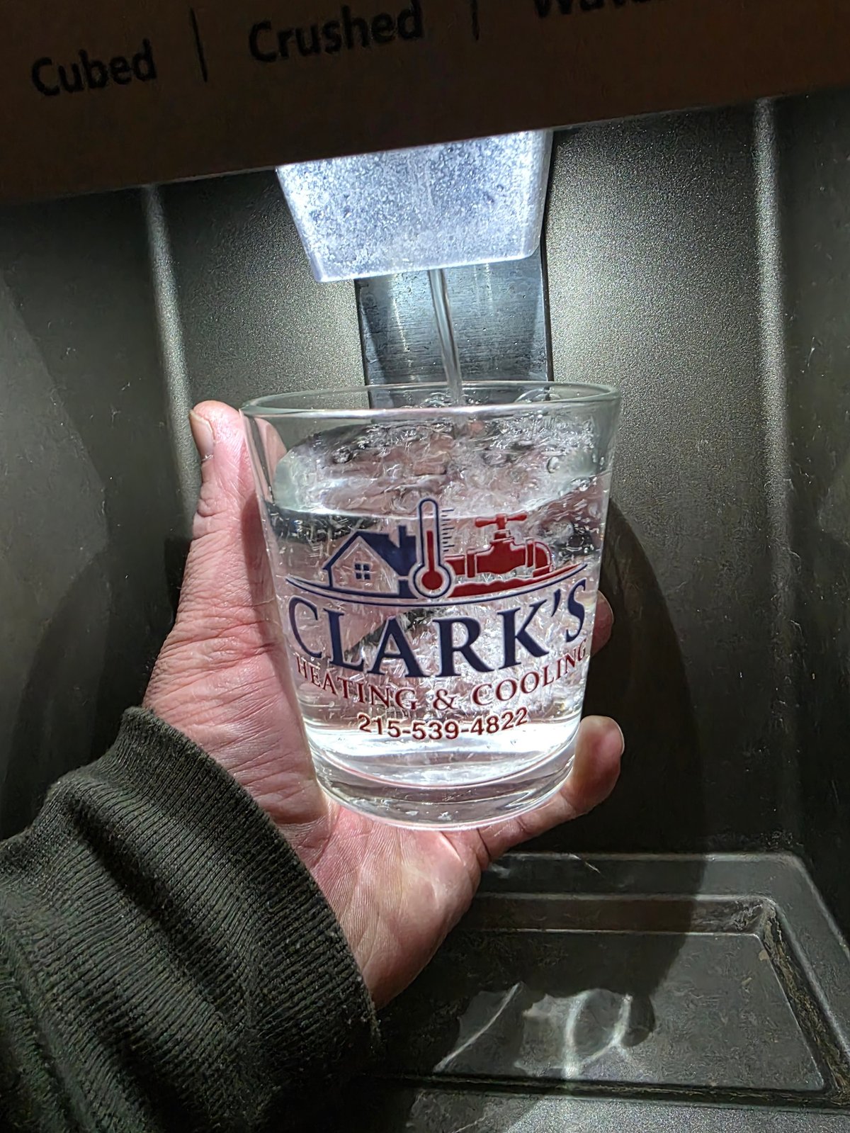 Hand holding a glass of ice water in front of an ice maker repaired by Clark's Heating and Cooling